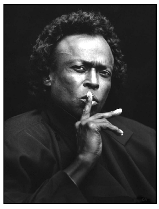 Iconic picture of Miles Davis holding his fingers up to his mouth in a quieting manner.